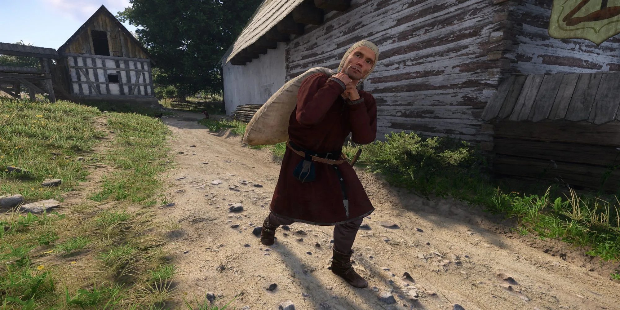 Nhân vật chính Henry đang vác một bao tải nặng trong môi trường nông thôn của Kingdom Come: Deliverance 2