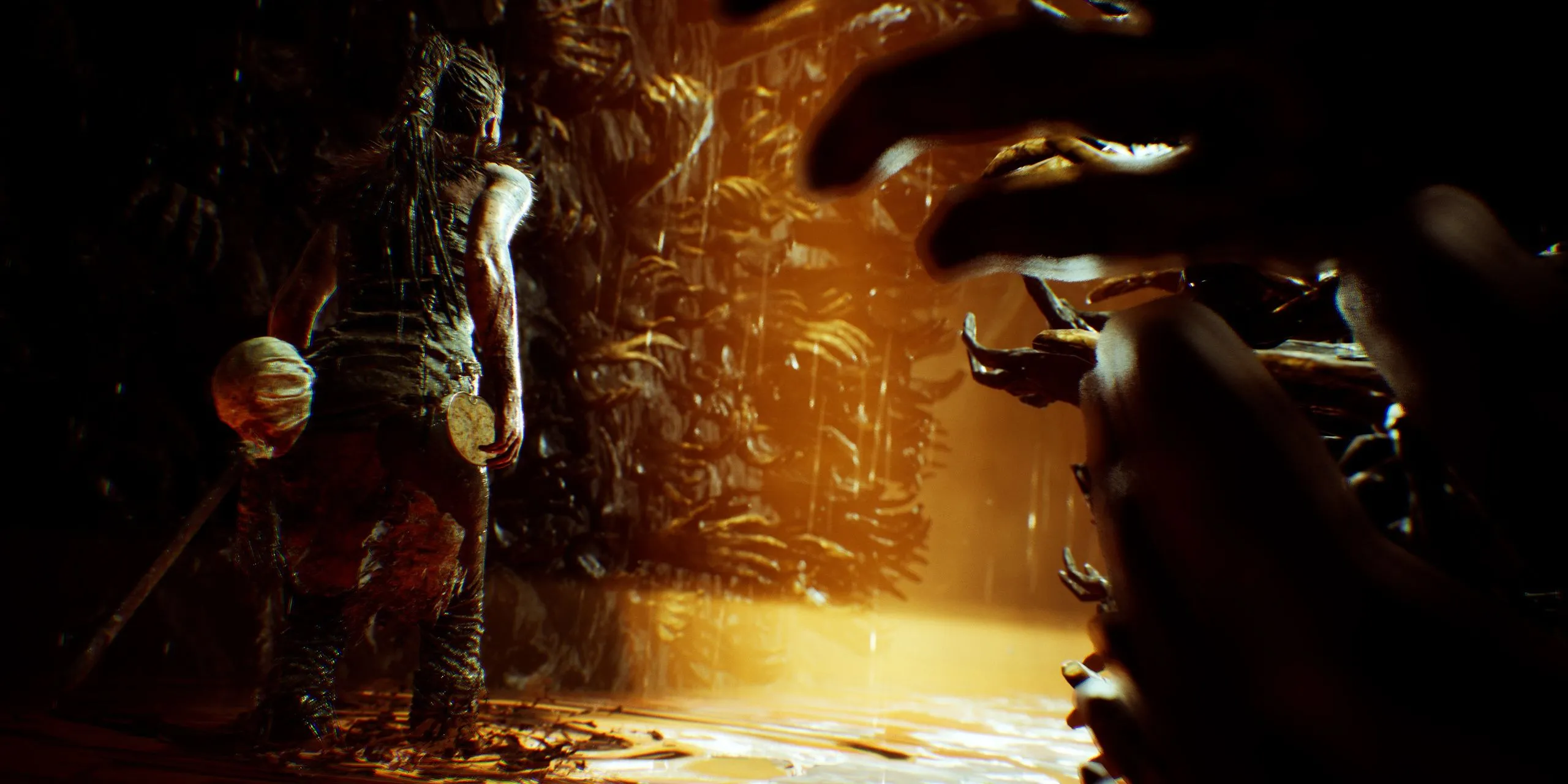 Senua đứng trước bức tường đầy những bàn tay trong Hellblade: Senua's Sacrifice, minh họa cho trải nghiệm âm thanh tái hiện chứng rối loạn tâm thần khi đeo tai nghe